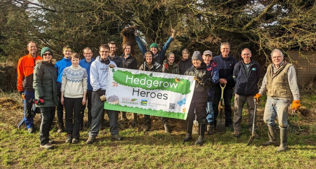 A group of volunteers gather around a Hedgerow Heroes banner looking happy