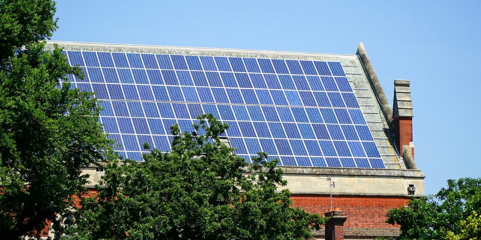 Solar panels on a large roof with trees in the foreground